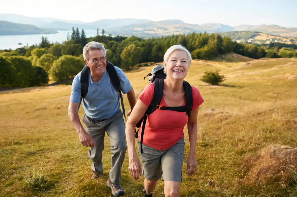 Senior couple smiles as they hike uphill with backpacks.