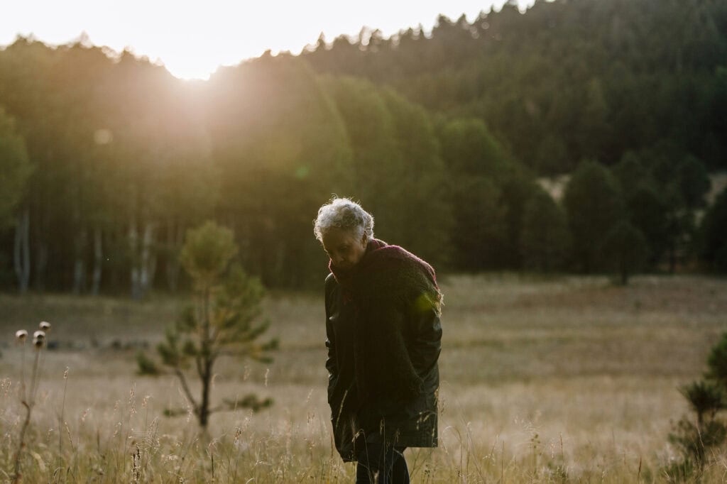 Older woman having a moment of reflection in the meadow of a Memorial Forest at sunset