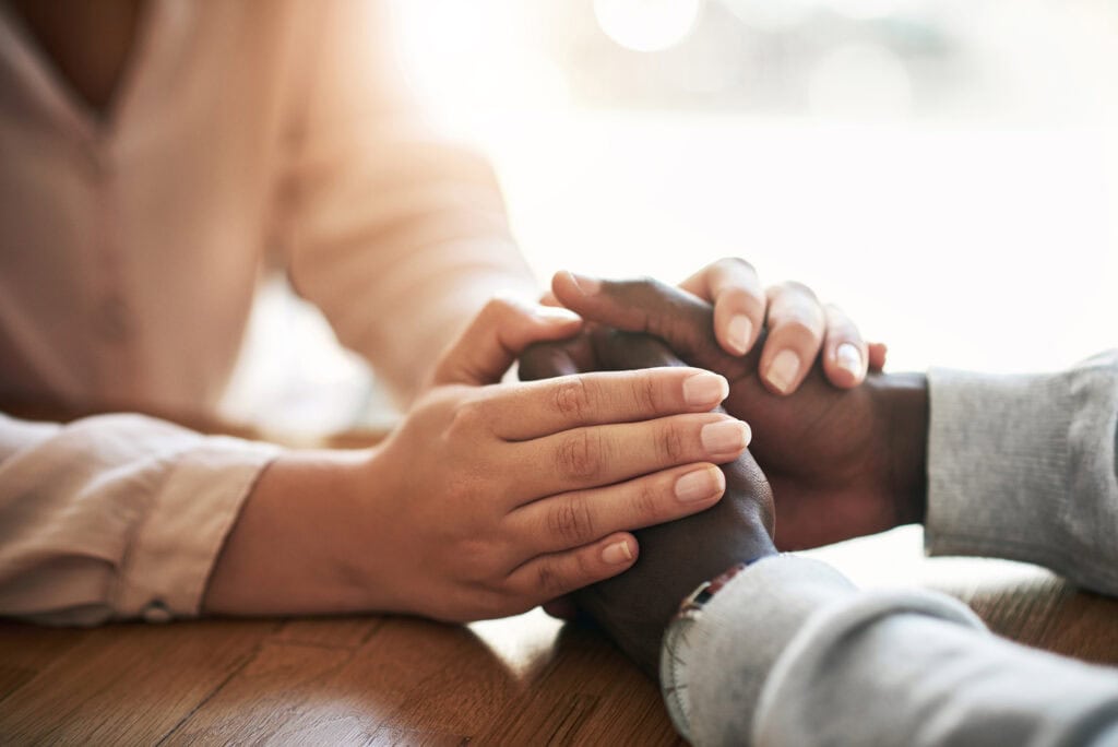 Closeup of hands of couple holding in loving support of care and comfort after grieving loss
