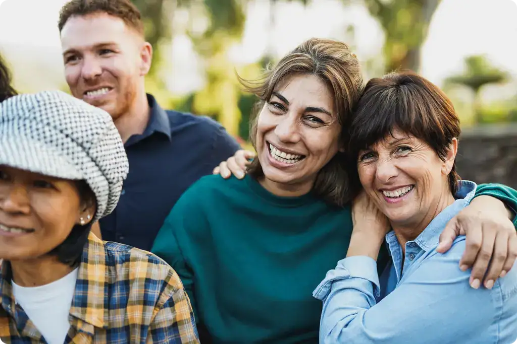 Multigenerational people having fun together outdoors focussed on senior women hugging each other while smiling on camera