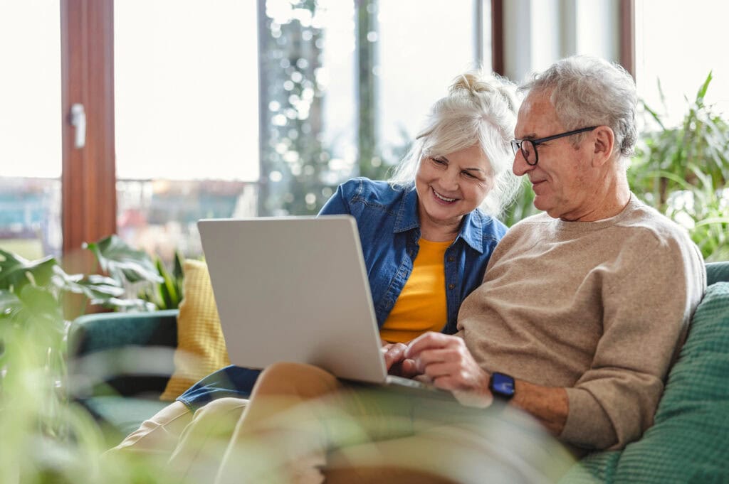 Senior couple reviewing end-of-life plans on laptop while sitting on sofa in living room at home