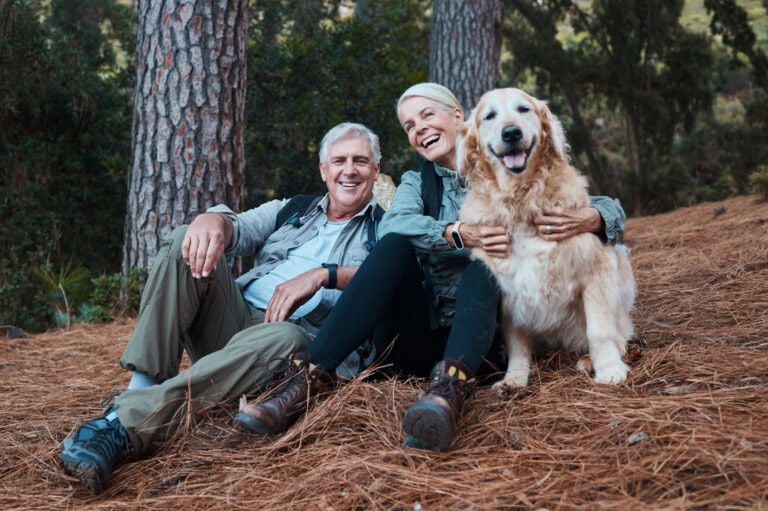 Senior couple with older dog sit together in memorial forest
