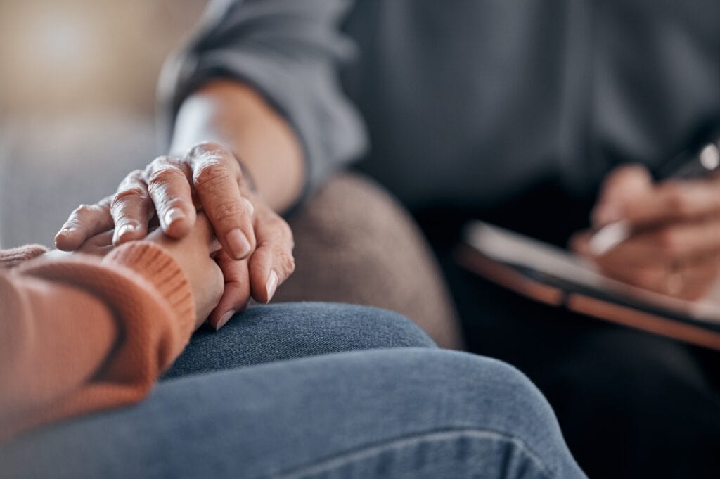 A close up of hands clasping in grief support as they write a letter announcing a death