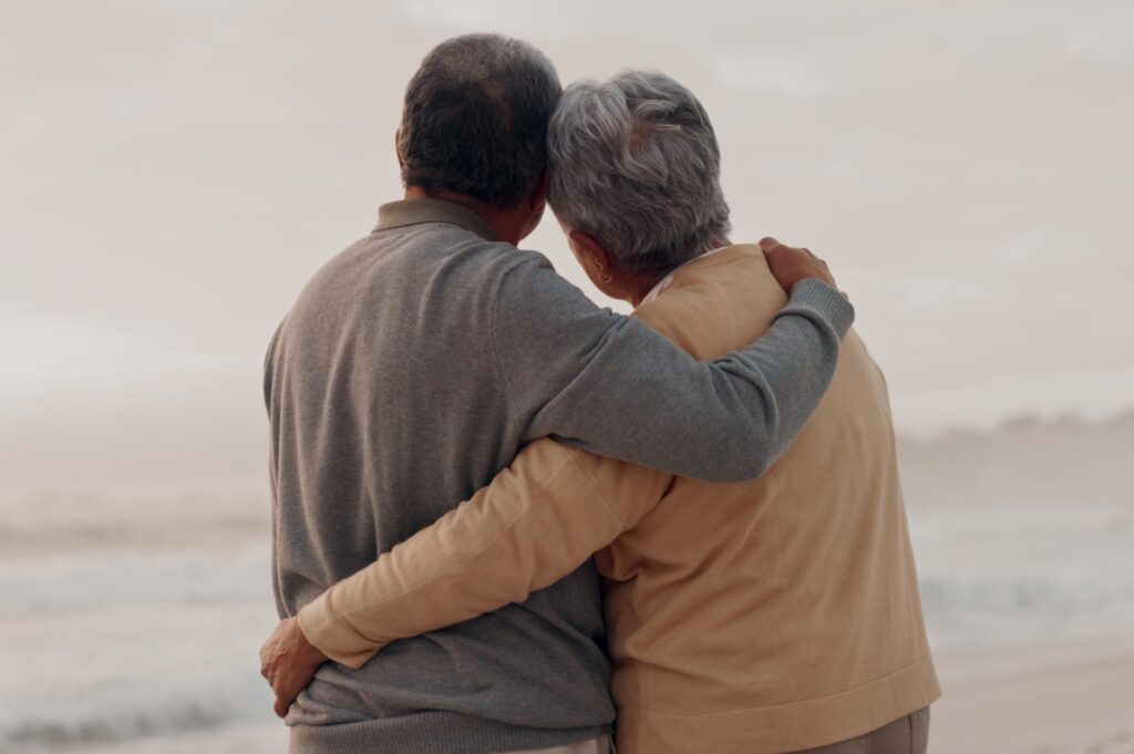 elderly couple embrace looking out at the sea