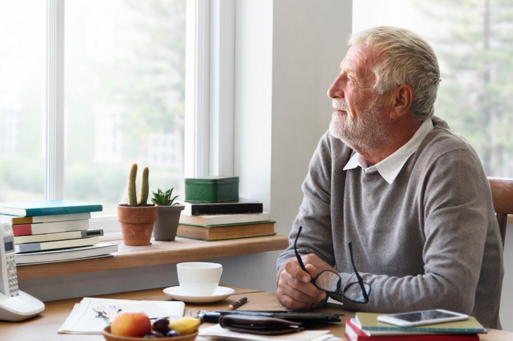 Senior man looking out window contemplating a memorial tribute
