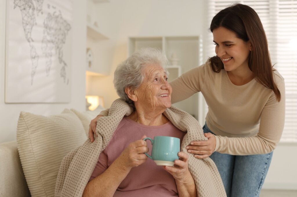 Granddaughter giving hot drink to her grandmother at home