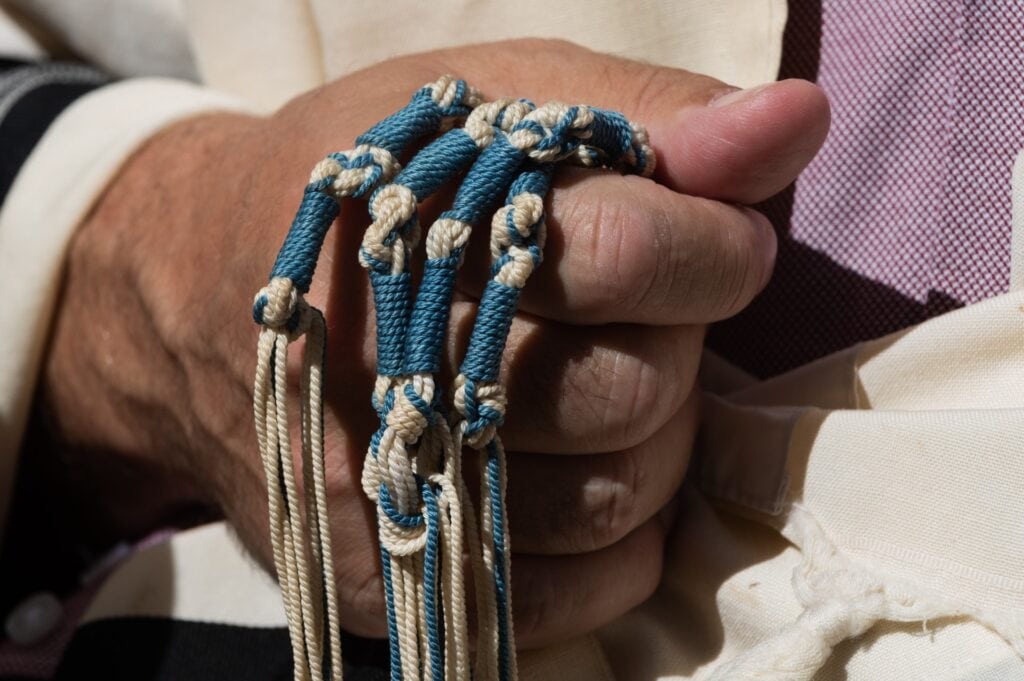 Jewish man holds blue strings while reciting prayers