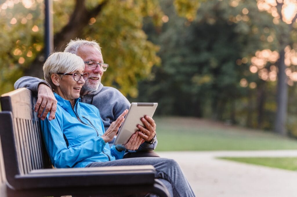 Older Couple sitting on park bench looking at prepaid cremation plans online