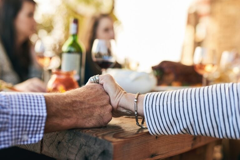 Close up of hands clasping with a large group of people gathering to celebrate the life of a loved one