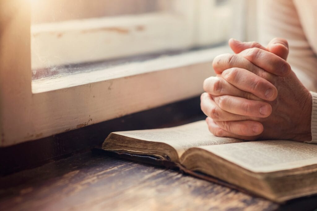 A bible with a prayer hands on top