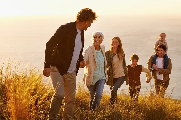 Multi-generational family walking up a grassy hill toward the ocean at sunset, symbolizing a peaceful return to nature and lasting family remembrance in a protected memorial forest.