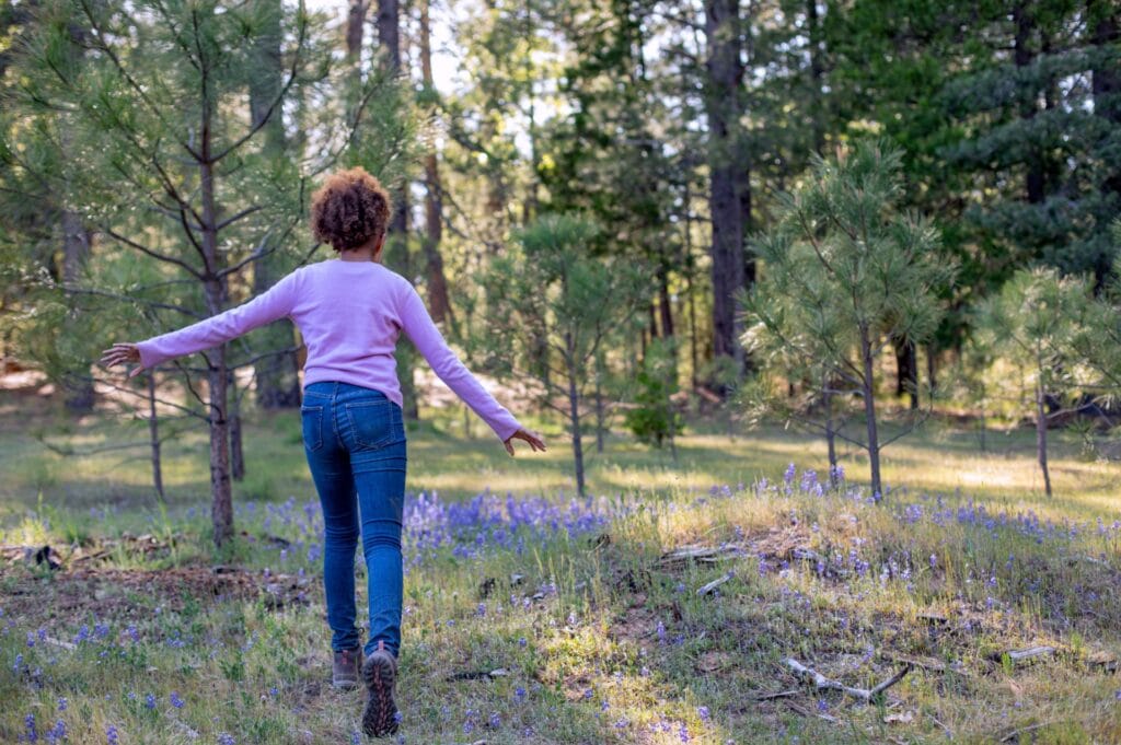 A girl running through a meadow with flowers in Yosemite Gateway Memorial Forest