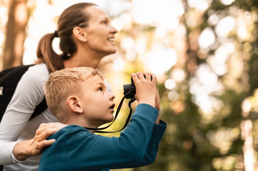 A mother and son birdwatching in a forest