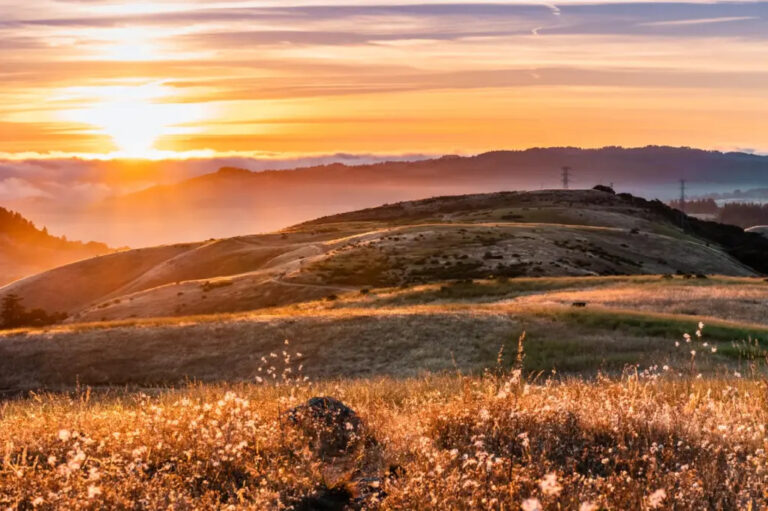 View of vibrant orange sunset sky over rolling dry grassy hills.