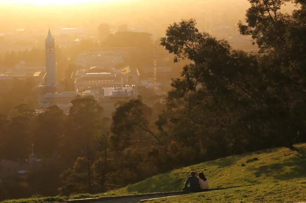 A couple sitting on the Berkeley Hill looks down at the UC Berkeley campus during sunset.