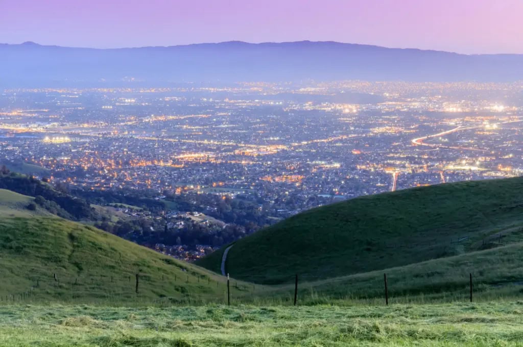 Hillside view overlooking a city at dusk as lights begin to illuminate the urban landscape.