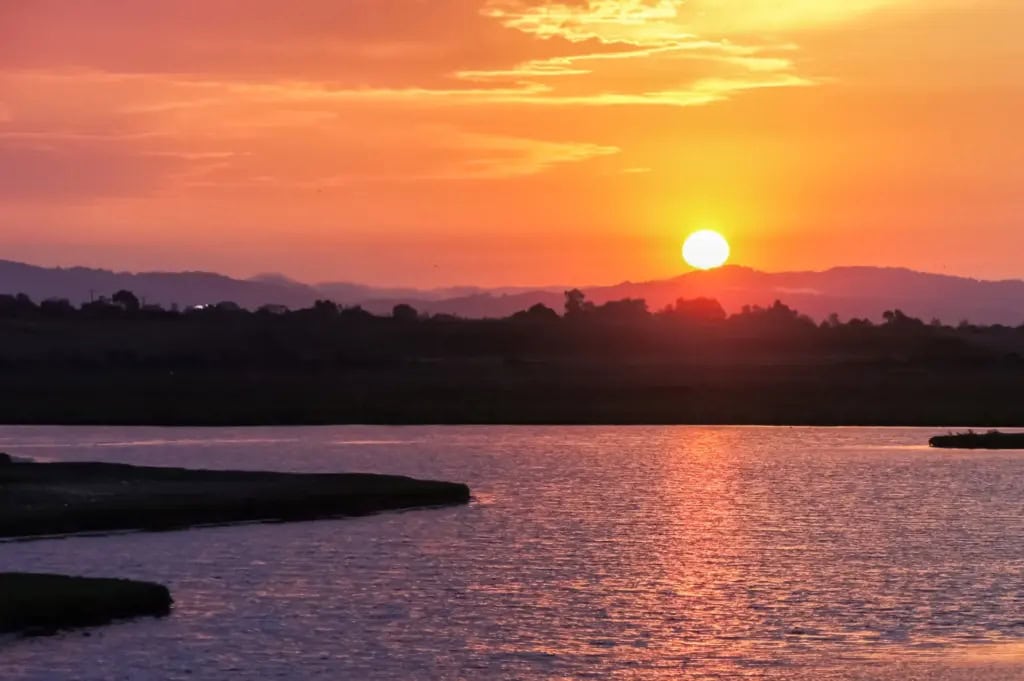 Sunset over calm water with golden light reflecting on the surface.