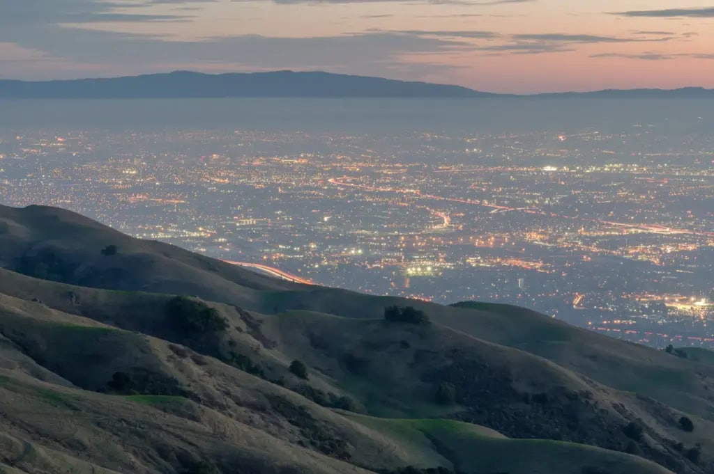 Hillside view overlooking a city at dusk as lights begin to illuminate the urban landscape.