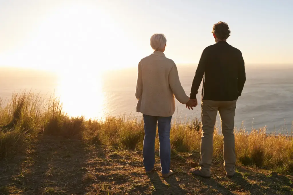 Older couple holds hands looking at the sunset over the ocean
