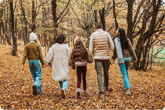 Back view of a family of five including a mother, father and three daughters walking hand-in-hand through the forest on a cool winter day.