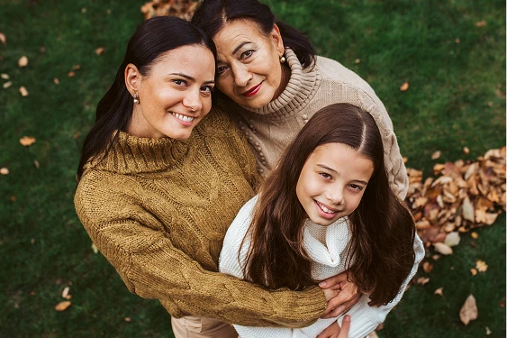 Portrait from above of a grandmother, mother, and daughter embracing and smiling in an outdoor setting.