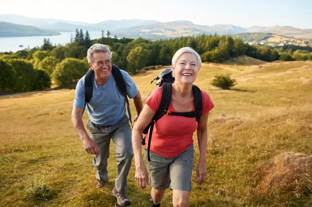 Senior couple smiles as they hike uphill with backpacks.