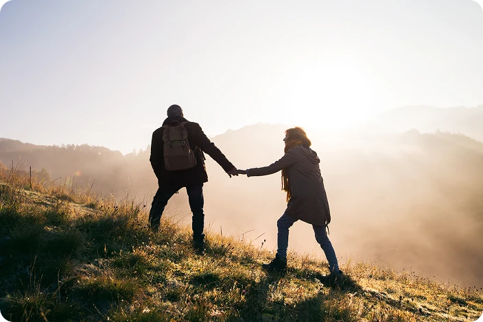 Couple silhouetted against a beautiful sunrise while walking up a hill together, representing the tranquility and peace of mind achieved through advance cremation plan