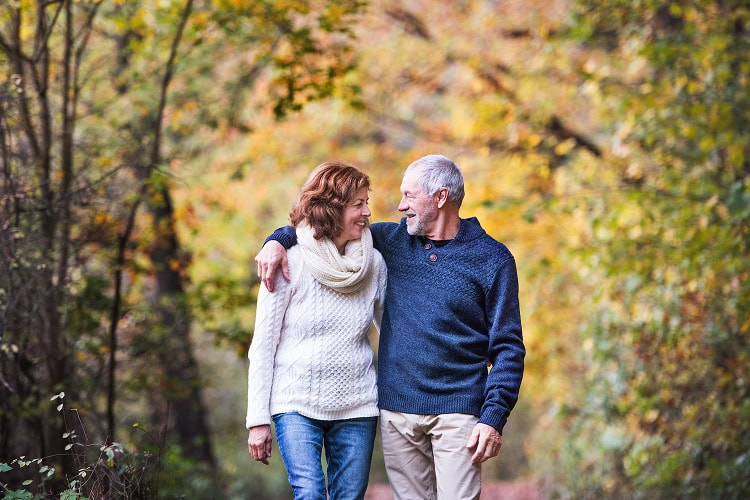 Older couple walking together in a protected forest during autumn, reflecting peace, connection, and planning ahead with confidence.