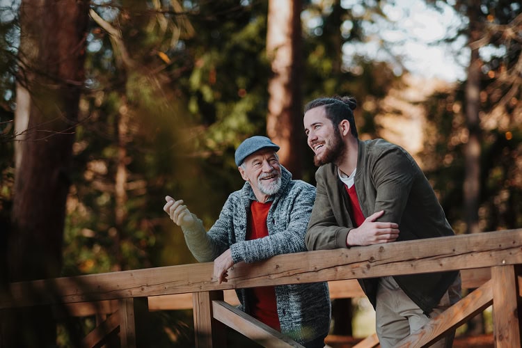 Older father and adult son standing together on a bridge, looking out at nature with trust and reflection.