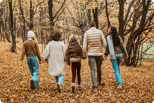 Back view of a family of five including a mother, father and three daughters walking hand-in-hand through the forest on a cool winter day.