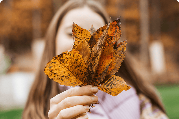 Woman holding a golden yellow leaf over her face.