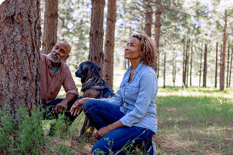 Husband and wife kneeling beside their memorial tree with their dog in a protected forest, symbolizing love, remembrance, and togetherness in nature.