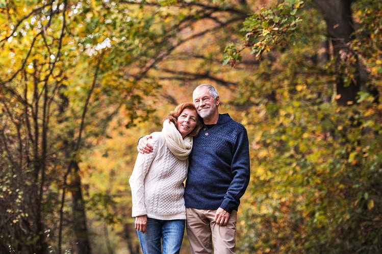 Smiling older couple embracing in an autumn forest setting.