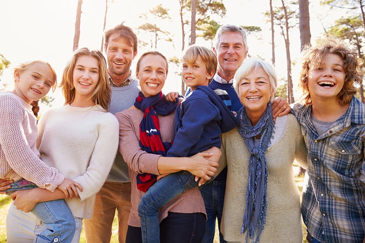 Portrait of a smiling multi-generational family in a forest setting on a sunny day.