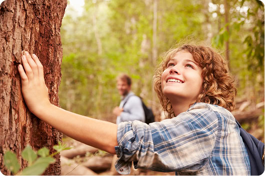A young boy looking up at the trees with his father in the background.
