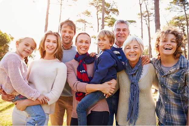 Portrait of a smiling multi-generational family in a forest setting on a sunny day.