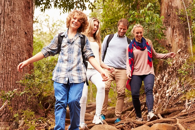 A family of four including a mother, father, and teen son and teen daughter walk along a trail in the forest.