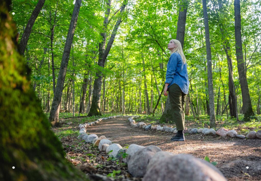 Woman in a memorial forest gazing up into the canopy, reflecting on a loved one and the cycle of life.