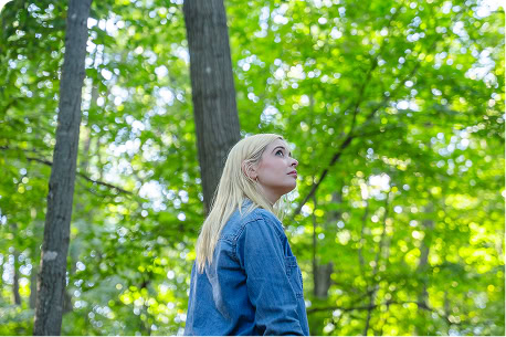 Woman gazing up into the canopy of trees in a memorial forest, reflecting quietly in a shared place of remembrance.