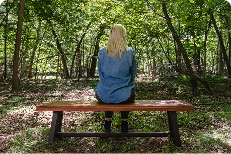 Woman sitting on a bench in a memorial forest, gazing into the distance during a quiet moment of reflection and connection.