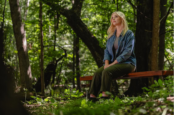 Woman sitting on a bench in a memorial forest, gazing into the distance during a quiet moment of reflection and connection.