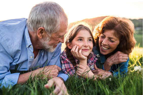 Senior couple relaxing on the grass with their granddaughter in spring, symbolizing the peace and protection that planning ahead provides.