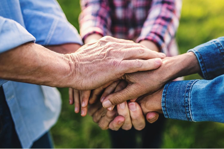 Hands of a young girl resting on top of her grandparents’ hands outdoors, symbolizing family support across generations.