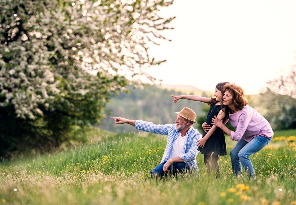 Senior couple with their granddaughter in a spring forest, pointing out nature and symbolizing a lasting place for future generations.