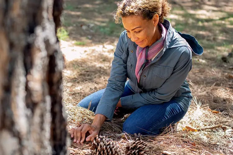 Woman kneeling beside her memorial tree with a hand on the memorial marker, reflecting quietly in the serenity of the forest.