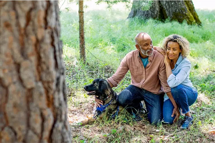 Husband and wife kneeling with their dog beside a memorial tree in a protected forest, symbolizing love, remembrance, and the bond that endures.