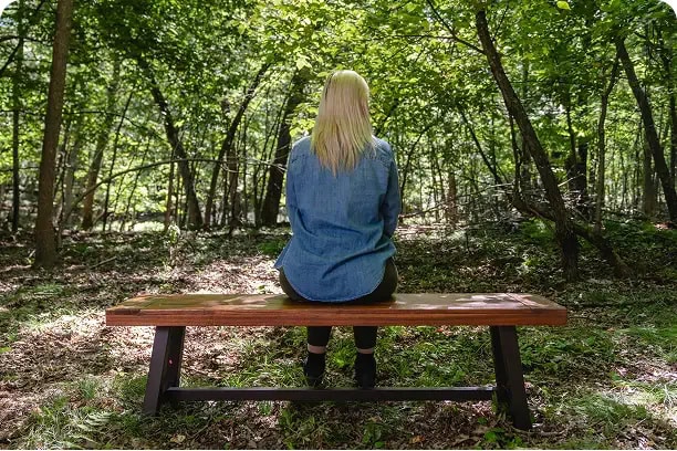 Woman sitting on a bench in a memorial forest, gazing into the distance during a quiet moment of reflection and connection.