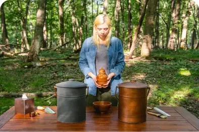 Woman standing at a memorial table with ashes, preparing to return them to the soil during a sustainable nature memorial.