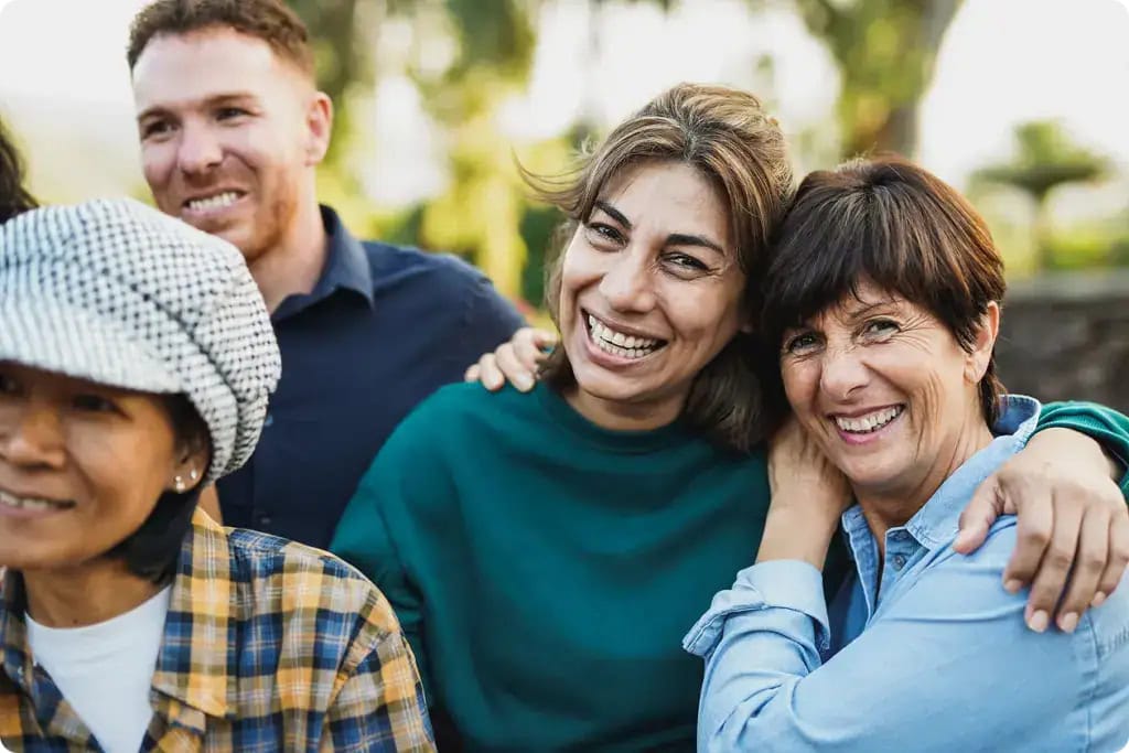 Multigenerational people having fun together outdoors focussed on senior women hugging each other while smiling on camera