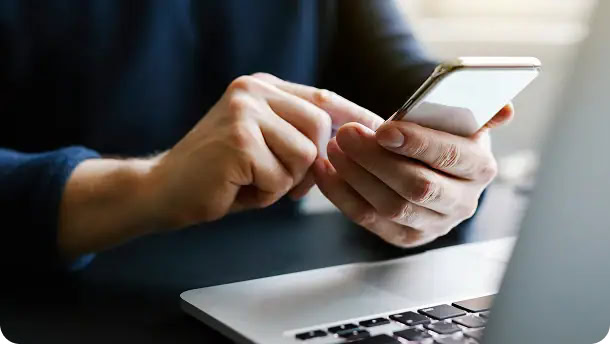 Man with finger on the screen using a mobile phone in front of computer at home